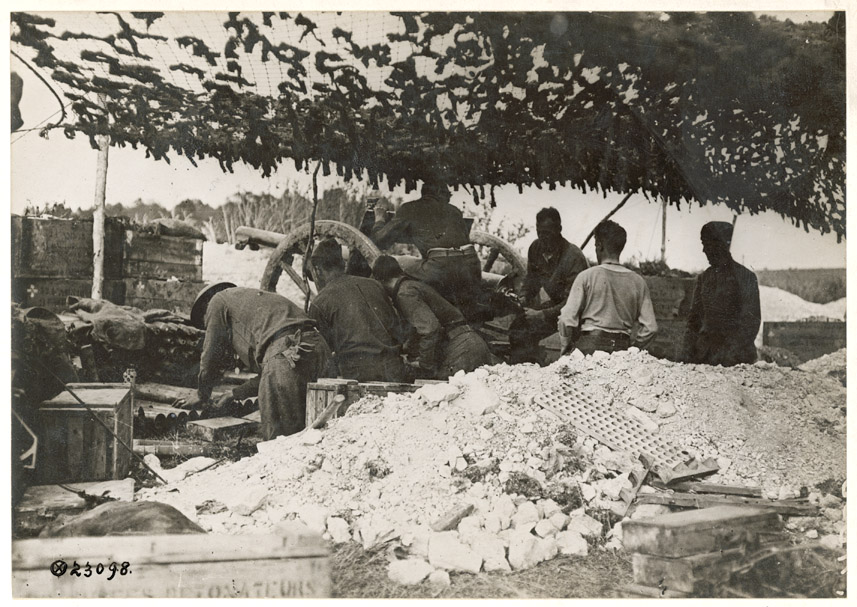 Soldiers work under a tent made of camouflage netting